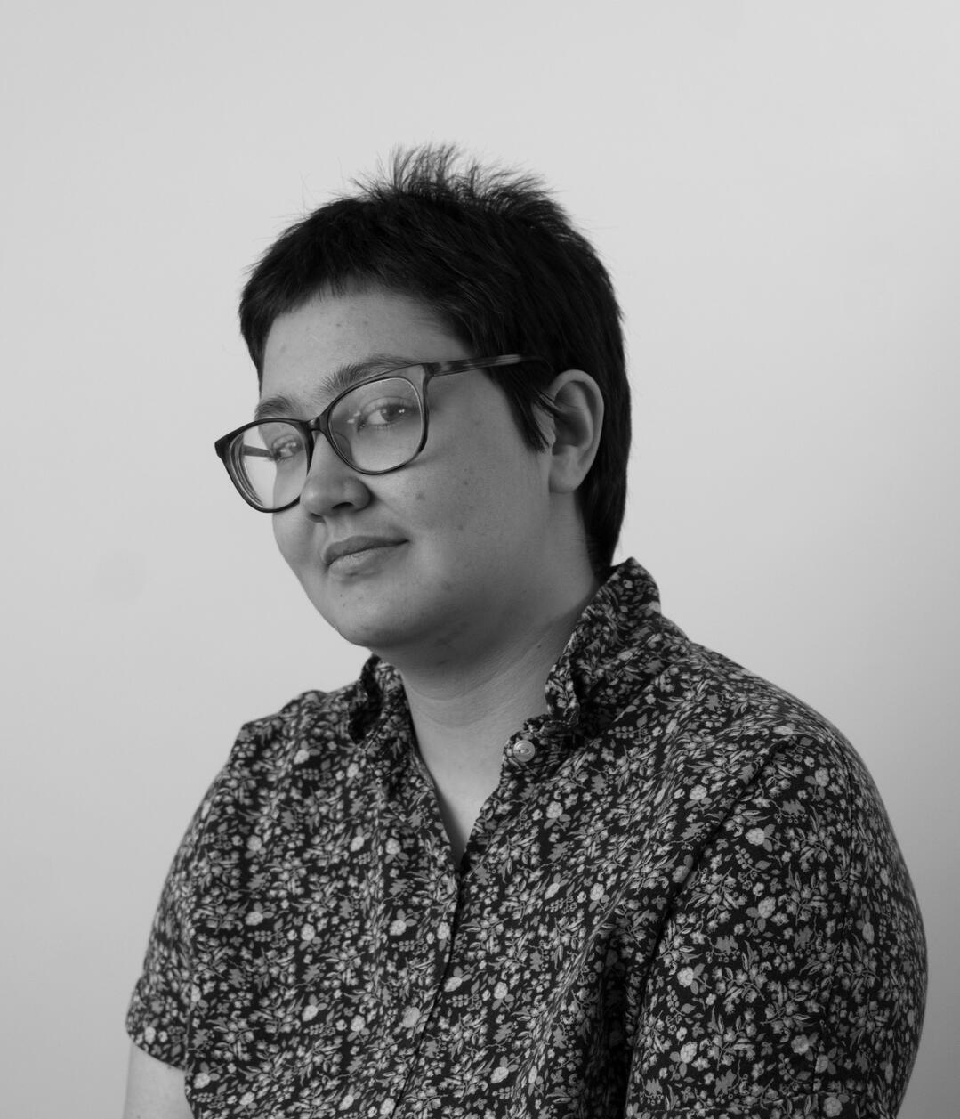 It's my headshot! The photo is in black and white. I'm growing out a buzzcut, and I'm wearing tortoiseshell glasses and a flower-print polo shirt.